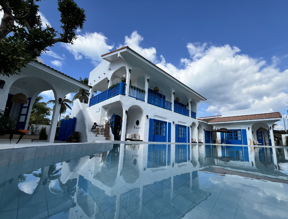 Casa Bella's whitewashed main building with blue shutters, reflected in the pool